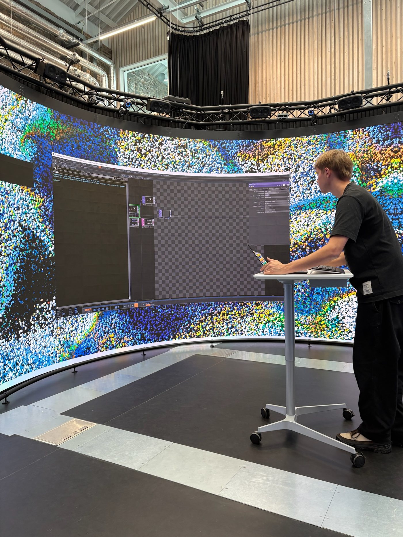 Photograph of a collaborator working at the Reality Emulator's curved panoramic screen, with TouchDesigner and generative test content displayed.